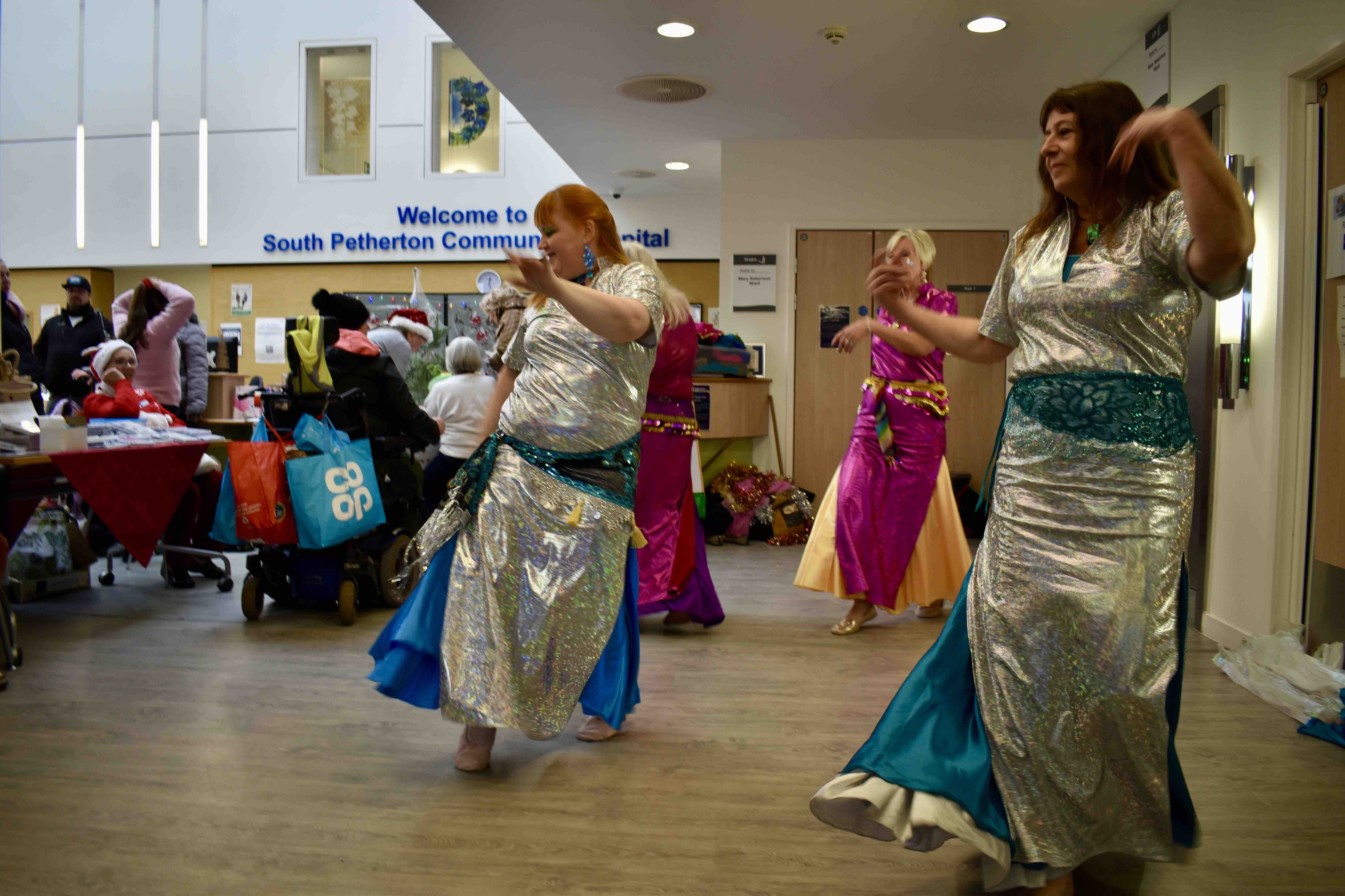 Women wearing long sparkling dresses as they dance, onlookers